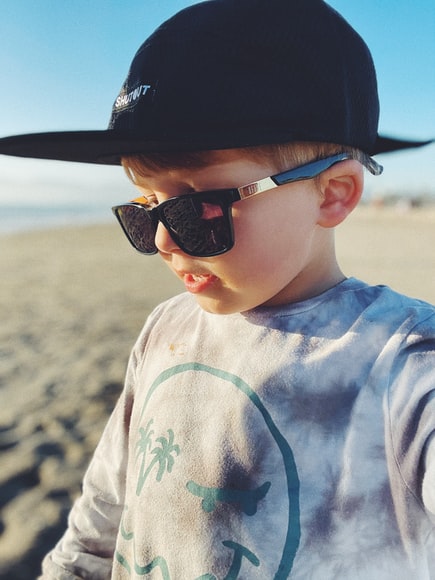 Young Boy with sunglasses and baseball cap and long sleeve shirt on the beach with the sun hitting their face
